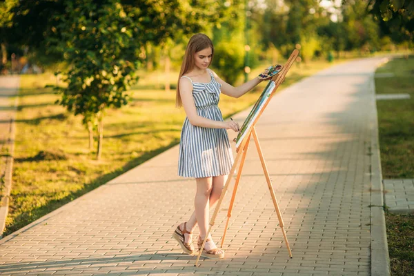 Blond vlasy dívka v šatech nakreslil obrázek v parku — Stock fotografie