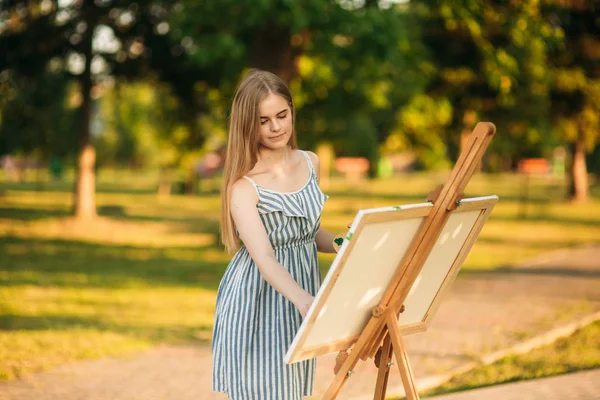 Блондинка в платье рисует картину в парке — стоковое фото