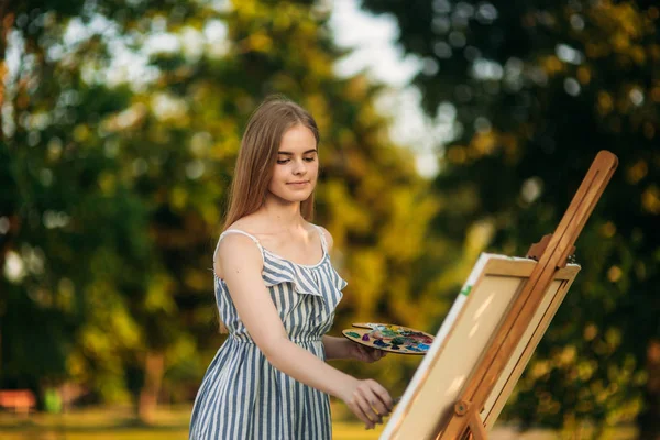 Blond vlasy dívka v šatech nakreslil obrázek v parku — Stock fotografie