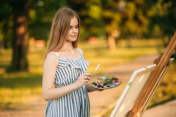 Retrato de chica rubia en vestido dibujando un cuadro en el parque — Foto de Stock