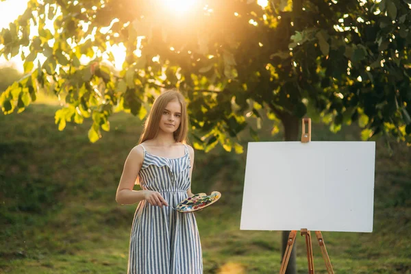 Krásná dívka umělce stojící v parku a drží paleta s barvami — Stock fotografie