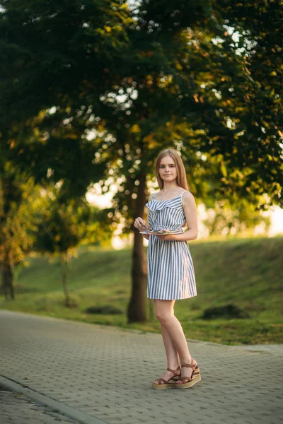 Bella artista ragazza è in piedi nel parco e tenendo tavolozza con vernici — Foto Stock