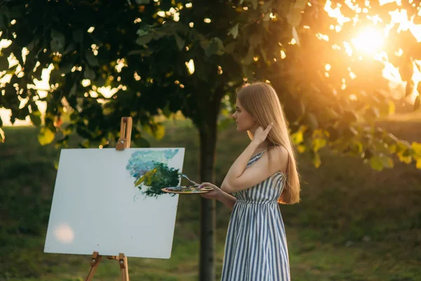 Retrato de bela artista menina está de pé no parque e segurando paleta com tintas — Fotografia de Stock