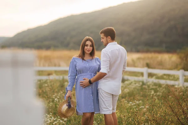 Mann und schwangere Frau stehen auf Feld in der Nähe des Hofes und umarmen sich — Stockfoto