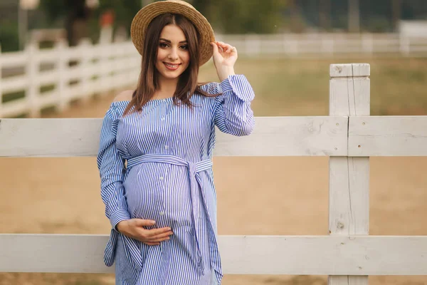 Prachtige zwangere vrouw in blauwe jurk staan buiten en zetten haar hand op de buik. Jonge en mooie toekomstige moeder — Stockfoto