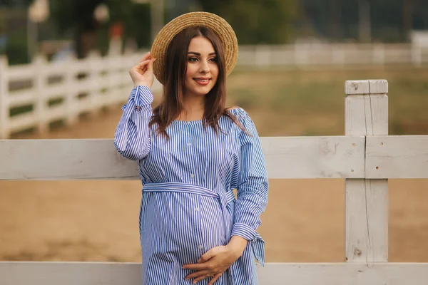 Superbe femme enceinte en robe bleue debout à l'extérieur et mettre sa main sur le ventre. Jeune et belle future mère — Photo