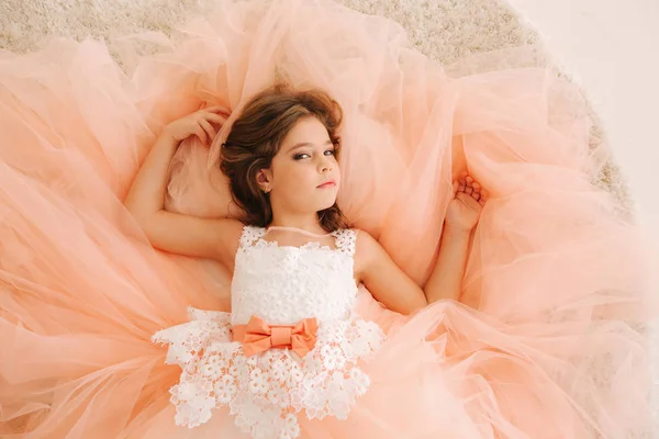 Фото маленькой девочки в студии. Маленькая красивая девочка с каштановыми волосами в персиковом платье — стоковое фото