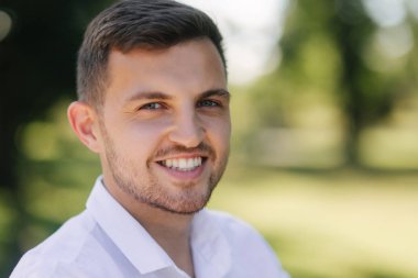 Beyaz bir gömlek ve şort gülümseme yakışıklı adam. Erkek model dışında. Park arka plan. Parkta yürüyen genç çekici adam