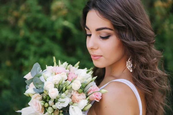 Hinreißende Frau im weißen Kleid Schleim. schönes Mädchen hält einen Blumenstrauß in den Händen — Stockfoto