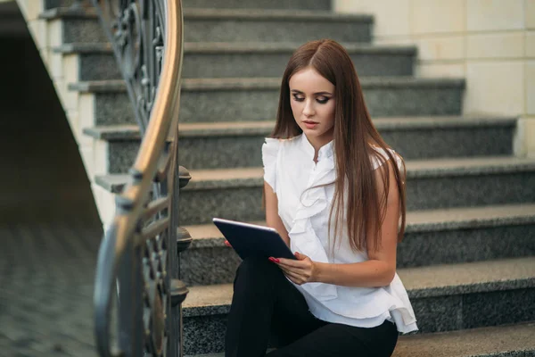 Genç ve çekici kadın merdivenlerde oturur ve tablet kullanır. Kadın tablette online oyunlar oynuyor — Stok fotoğraf