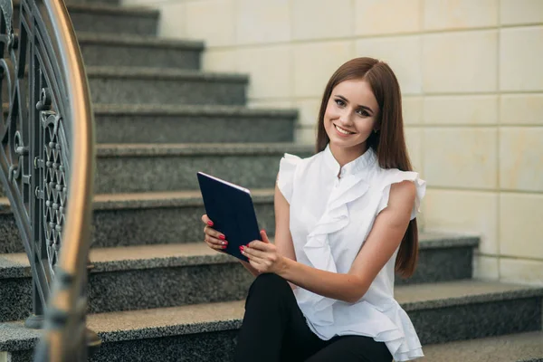 Genç ve çekici kadın merdivenlerde oturur ve tablet kullanır. Kadın tablette online oyunlar oynuyor — Stok fotoğraf