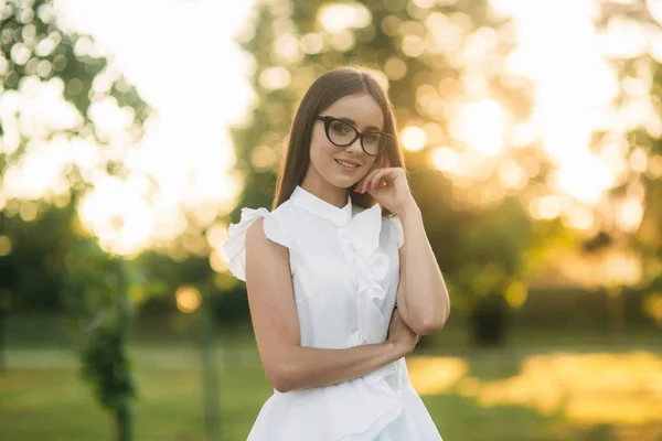 Elegant woman in glasses standing in the park and looking through glasses. Female model
