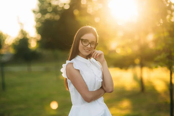 Elegante donna in occhiali in piedi nel parco e guardando attraverso gli occhiali. Modello femminile — Foto Stock