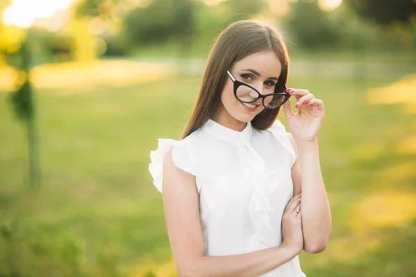 Κομψή γυναίκα με γυαλιά που στέκεται στο πάρκο και κοιτάζει μέσα από τα γυαλιά. Θηλυκό μοντέλο — Φωτογραφία Αρχείου