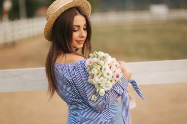 Georgeus kadın çiftlik önünde stand ve bir buket çiçek elinde tut. Beautuful buket. Kadın mavi elbise ve örme şapka