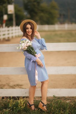 Georgeus kadın çiftlik önünde stand ve bir buket çiçek elinde tut. Beautuful buket. Kadın mavi elbise ve örme şapka