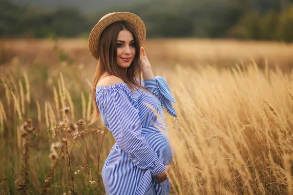 Tendre femme enceinte marcher dans un champ. Dame avec chapeau en robe bleue. Détends-toi. Femme attend un bébé — Photo