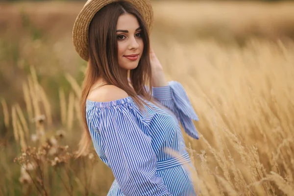 Mujer embarazada tierna caminar en un campo. Señora con sombrero en vestido azul. Relájate. La mujer está esperando un bebé. —  Fotos de Stock