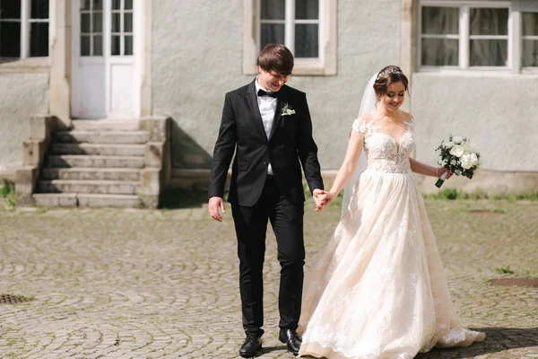 Feliz casal recém-casado em roupas de casamento andando perto do castelo — Fotografia de Stock