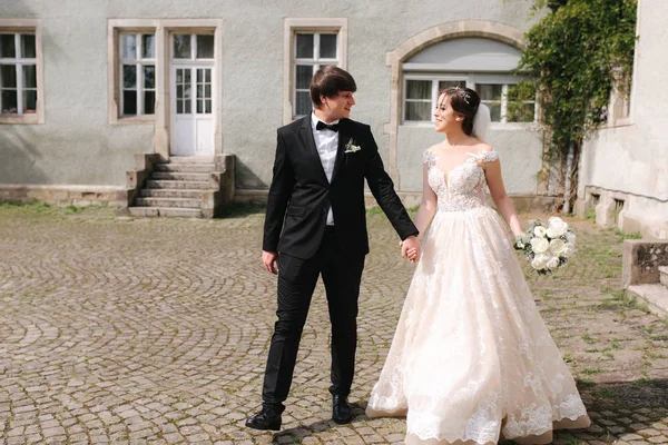 Feliz casal recém-casado em roupas de casamento andando perto do castelo — Fotografia de Stock