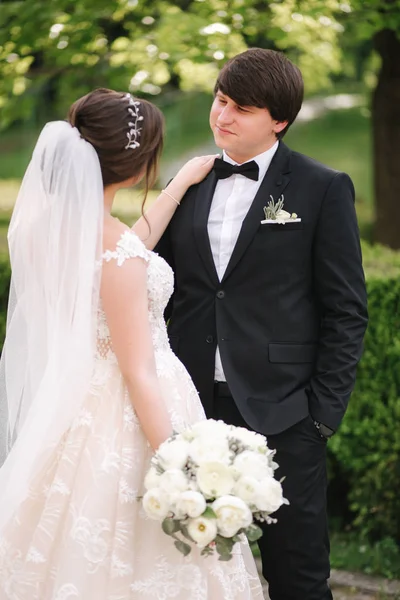 Sposa elegante in bellissimo abito da sposa bianco con bello sposo nel parco. Sfondo verde — Foto Stock