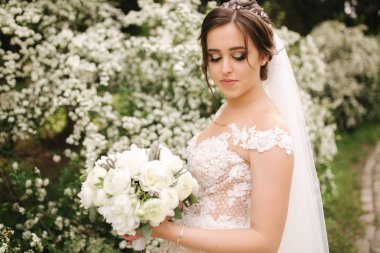 Muhteşem gelinlik Büyüleyici gelin tutun buket ve çiçek açan ağaçların önünde durmak