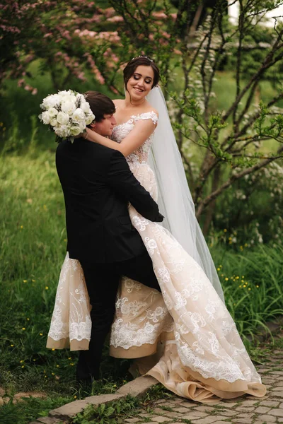 Bella coppia di nozze a piedi nel parco. Sposa con abito lungo bianco ed elegante sposo. Albero rosa — Foto Stock