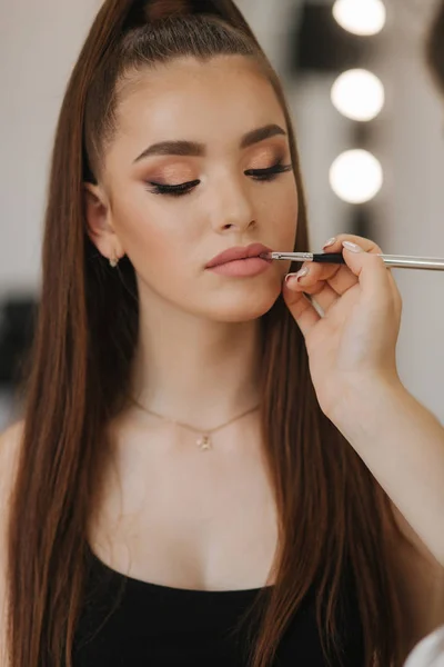 Makeup artysta stosuje szminkę. Ręka makijażu mistrza, malowanie usta młodego modelu rude piękno. Makijaż w procesie — Zdjęcie stockowe