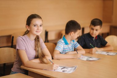 Eğitim, ilkokul. Öğrenme ve insan konsepti - kalemi ve not defterleri olan bir grup okul çocuğu sınıfta yazı sınavı