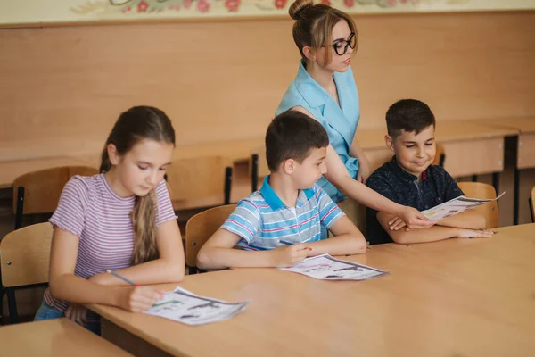 Teacher helping school kids writing test in classroom. education, elementary school, learning and people concept — Stock Photo, Image