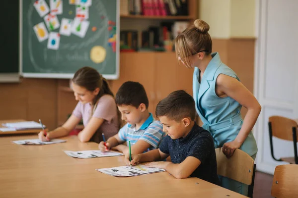 Profesor ayudando a los niños de la escuela a escribir prueba en clase. educación, escuela primaria, aprendizaje y concepto de personas — Foto de Stock