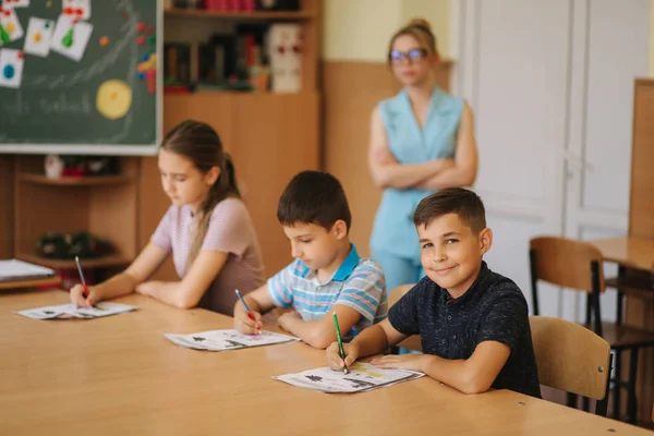 Teacher helping school kids writing test in classroom. education, elementary school, learning and people concept — Stock Photo, Image