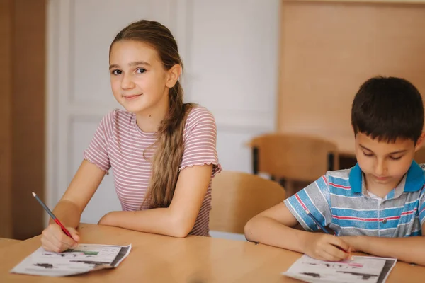 Boy and girl sitting at desk and writing a text — Stock Photo, Image