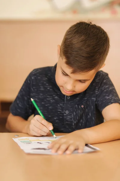 Koncentrerad skolpojke sitter vid skrivbordet och skriver i träningsbok — Stockfoto