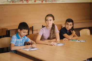 Eğitim, ilkokul. Öğrenme ve insan konsepti - kalemi ve not defterleri olan bir grup okul çocuğu sınıfta yazı sınavı