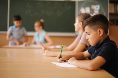 Eğitim, ilkokul. Öğrenme ve insan konsepti - kalemi ve not defterleri olan bir grup okul çocuğu sınıfta yazı sınavı
