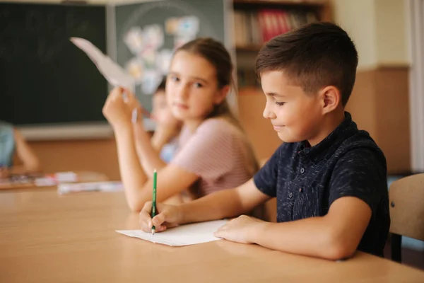 Grupo de crianças da escola com canetas e cadernos teste de escrita em sala de aula. educação, escola primária, aprendizagem e conceito de pessoas — Fotografia de Stock