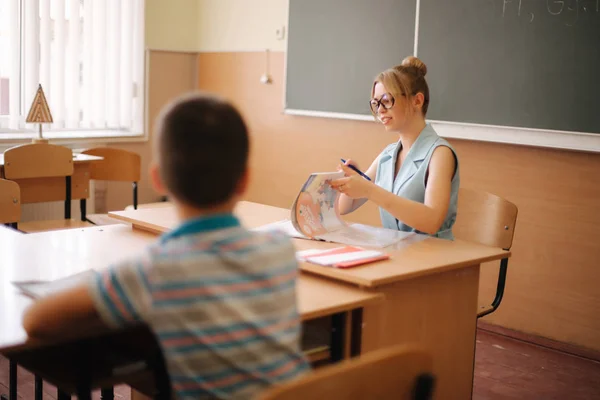 Όμορφη δασκάλα στην τάξη κάθεται στο γραφείο και ρωτάει τα παιδιά. εκπαίδευση, Δημοτικό σχολείο, μάθηση και αντίληψη των ανθρώπων — Φωτογραφία Αρχείου