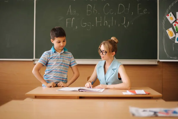 Красивая учительница в классе сидит за столом и спрашивает детей. образование, школа, обучение и человеческая концепция — стоковое фото