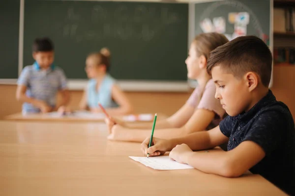 Educação, escola primária. Aprendizagem e conceito de pessoas - grupo de crianças da escola com canetas e cadernos teste de escrita em sala de aula — Fotografia de Stock