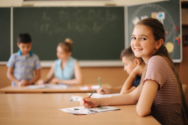 Education, elementary school. Learning and people concept - group of school kids with pens and notebooks writing test in classroom