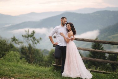 Sevimli gelin dağlarda onu yakışıklı damat sarılmak. Güzel düğün çift yürüyüş. Yeşil gackground