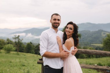 Sevimli gelin dağlarda onu yakışıklı damat sarılmak. Güzel düğün çift yürüyüş. Yeşil gackground