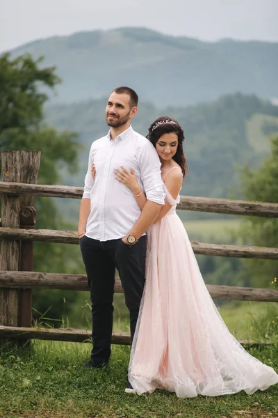 Charmante Braut umarmt ihren hübschen Bräutigam in den Bergen. schönes Hochzeitspaar zu Fuß. Grünes Pflaster — Stockfoto