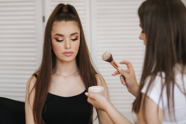 Kadın makyaj ustası bir toz fırça kullanın. Güzellik stüdyosunda güzel bir model. Profesyonel makyaj sanatçı bitirmek moda maleup. Beyaz katlanır ekranın arka planı