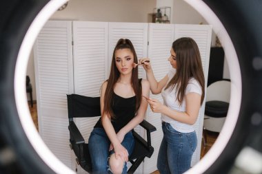 Fotoğraf makyaj sanatçısının yüzük lambası çekici genç kız için bir makyaj yapıyor olsa. Beyaz katlanır ekranın arka planı