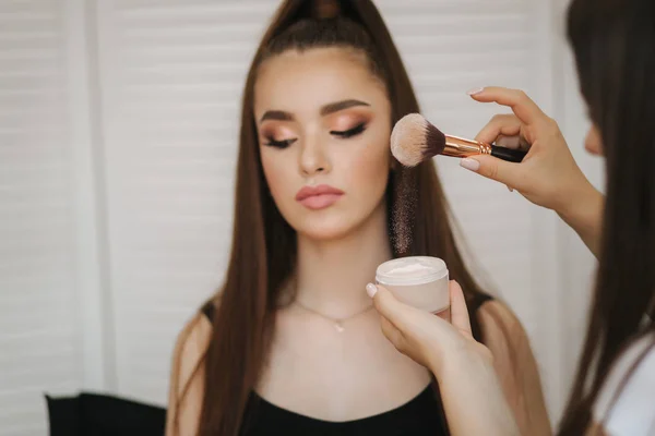 Maestro trucco femminile utilizzare una spazzola a polvere. Bella modella in studio di bellezza. Trucco professionale artista finitura malup moda. Sfondo dello schermo pieghevole bianco — Foto Stock