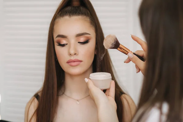 Maestro trucco femminile utilizzare una spazzola a polvere. Bella modella in studio di bellezza. Trucco professionale artista finitura malup moda. Sfondo dello schermo pieghevole bianco — Foto Stock