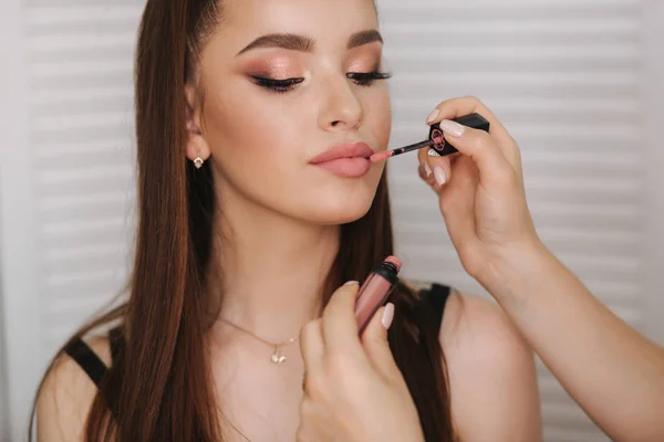 Hand of makeup artist hold lipstick brush and doing makeup. Beautiful model smile. Background of white folding screen