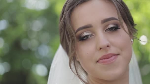 Affascinante sposa in splendido abito da sposa tenere bouquet e stare di fronte a alberi in fiore — Video Stock